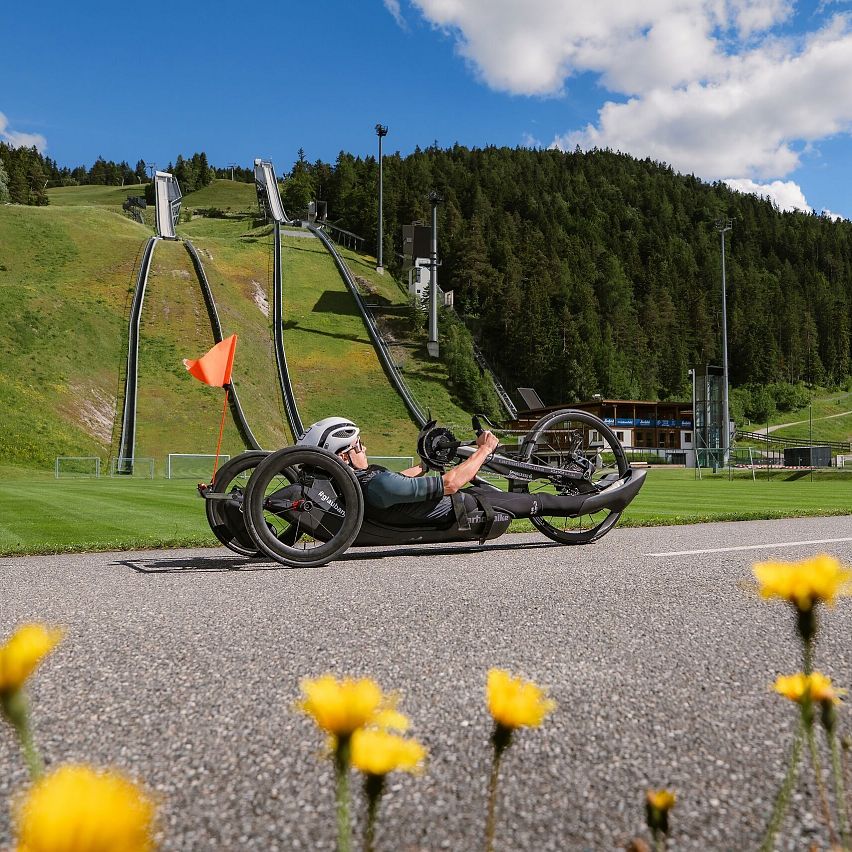 Ein Radfahrer auf einem handbetriebenen Dreirad in der Region Seefeld, umgeben von Wiesen und Bergen.
