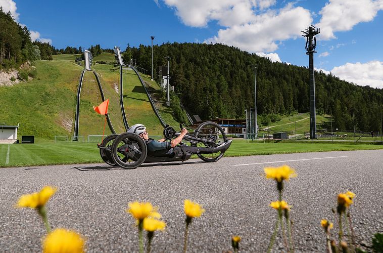 Radfahrer auf einem Liegerad in der Region Seefeld, grüne Wiesen und Berge im Hintergrund.