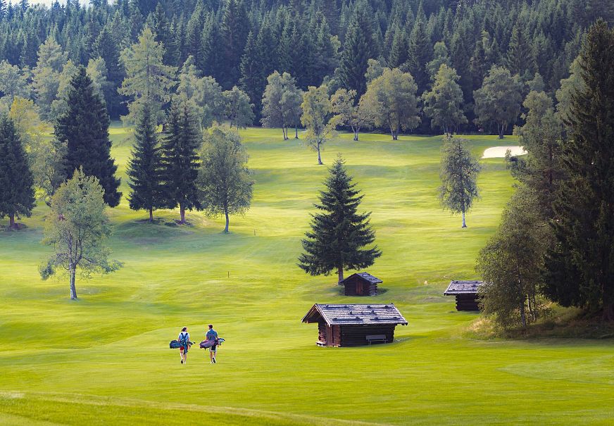 Golfen im GC Wildmoos im Sommer_zwei Golfer laufen über Wiese bei Hütten
