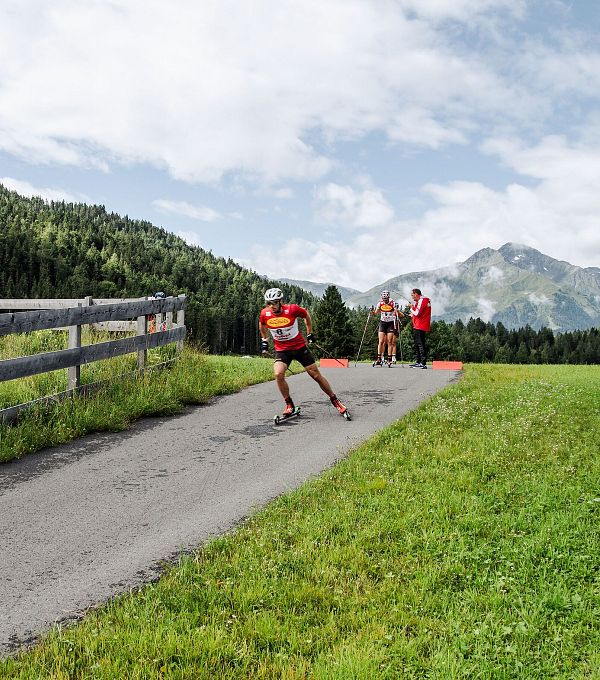 Sportler auf Rollski in der Region Seefeld fährt eine asphaltierte Strecke entlang eines grünen Feldes.