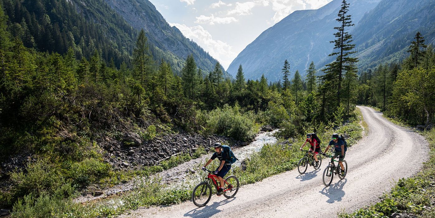 Radfahrer im grünen Tal der Region Seefeld, umgeben von Bergen, auf einer Kiesstraße.