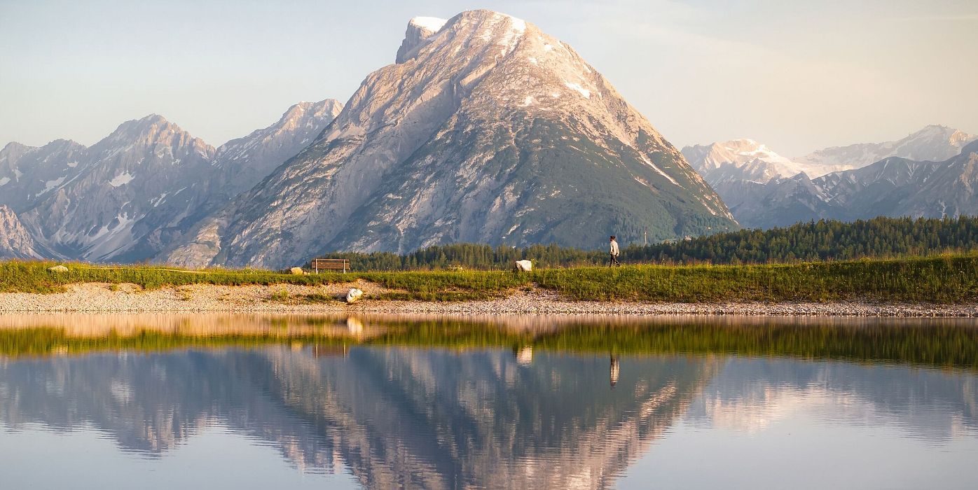 Drohnenaufnahme Gschwandtkopf Speichersee - Person läuft entlang des Speichersees mit Hohe Munde im Hintergrund