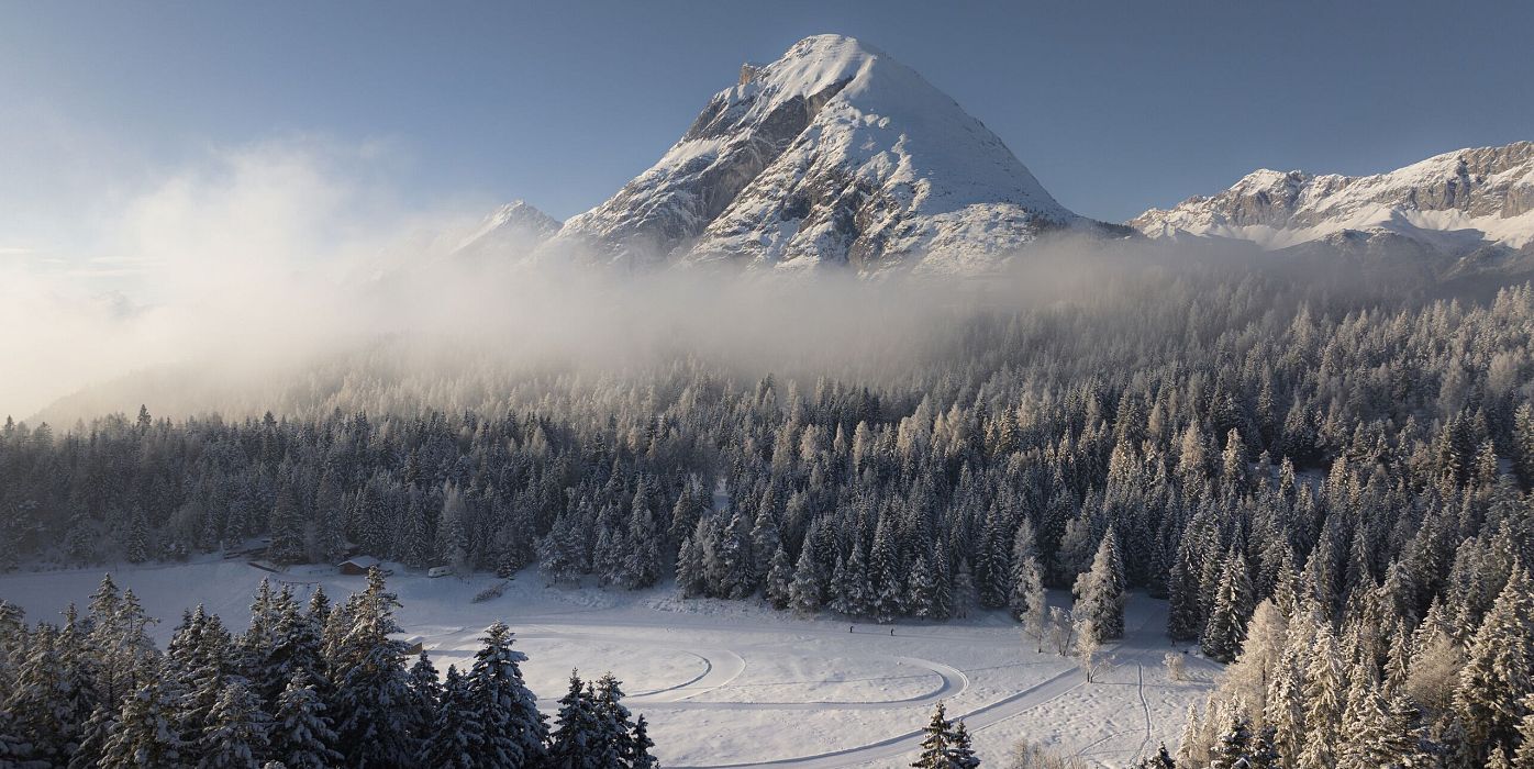 Schneebedeckter Berg und Wald in der Region Seefeld; klarer Winterhimmel, leichter Nebel. Ideal für Wintersport.