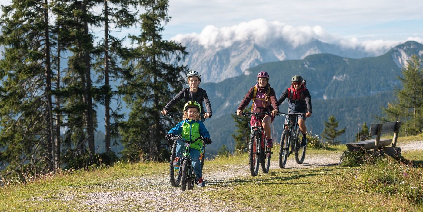 Familie beim Mountainbiken auf einem Pfad in der Region Seefeld, mit Bergen im Hintergrund.