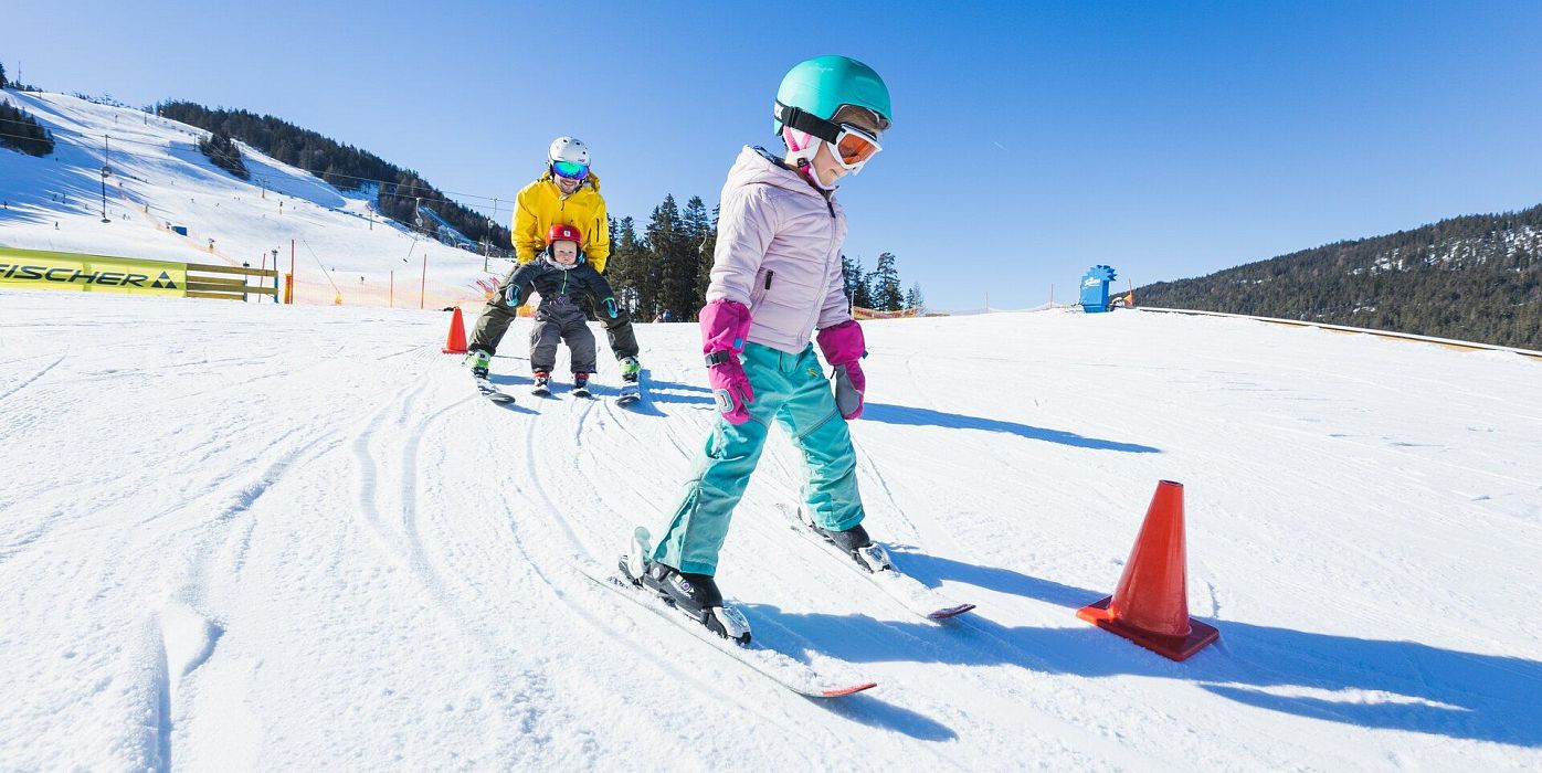 Kinder im Skikurs in der Region Seefeld. Sie fahren eine verschneite Piste hinunter, begleitet von einem Skilehrer.