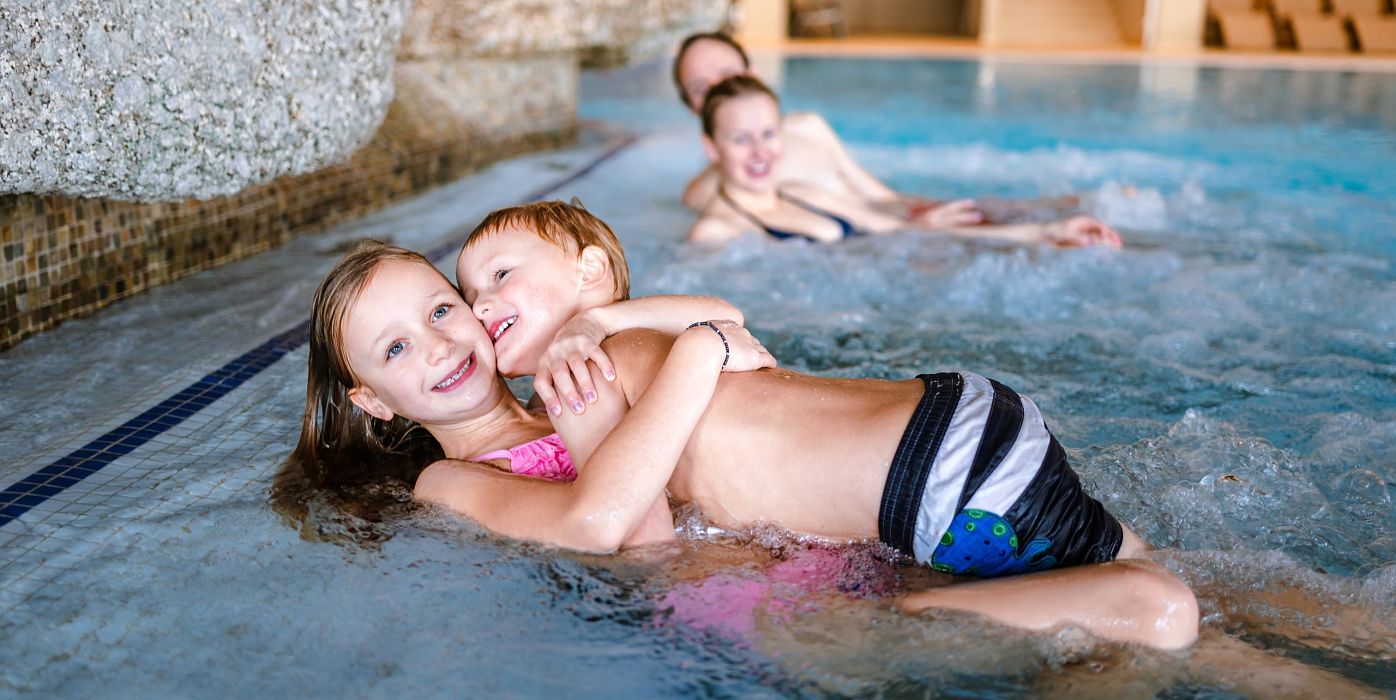 Zwei Kinder im Wasser eines Schwimmbades, das Mädchen umarmt den Jungen.