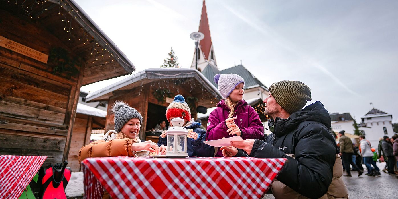 Drei Personen sitzen an einem Tisch auf einem Weihnachtsmarkt.