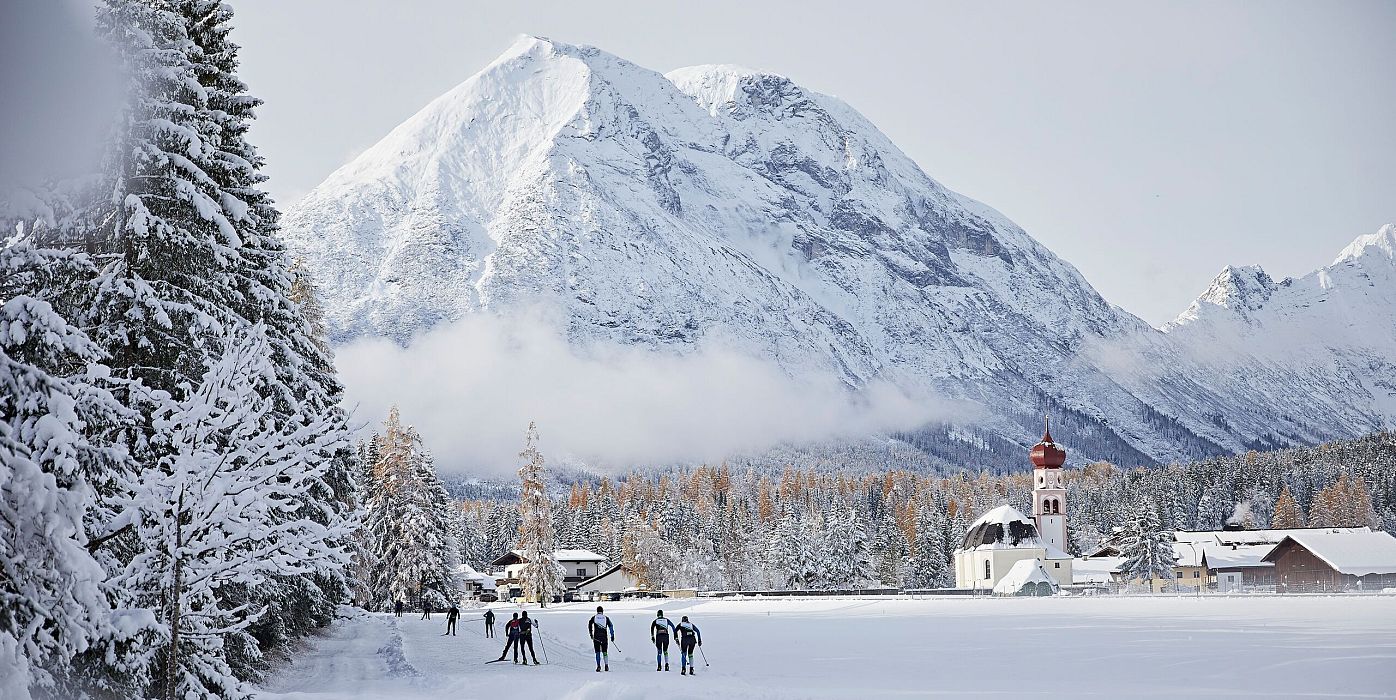 Langläufer in der Region Seefeld vor schneebedeckten Bergen. Winterlandschaft mit Bäumen und kleinem Gebäude im Hintergrund.