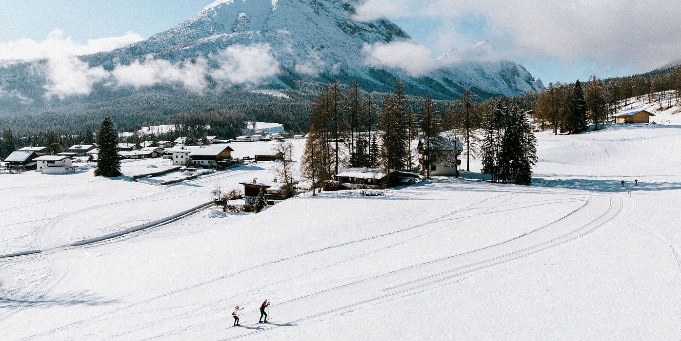 Zwei Langläufer in der Region Seefeld, umgeben von verschneiten Bergen und Wald.