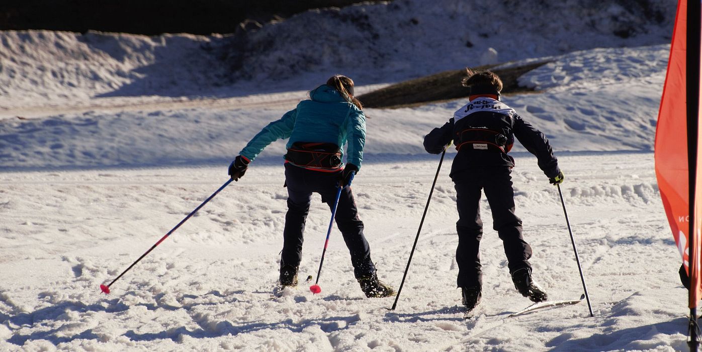 Zwei Kinder beim Langlaufen im Schnee mit Skistöcken, sonnige Winterlandschaft.