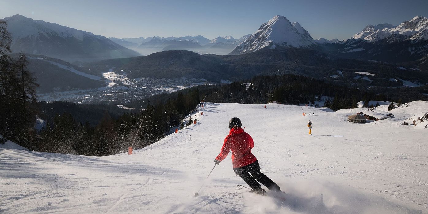 Skifahrer fährt Piste in der Region Seefeld hinunter, Alpen im Hintergrund.