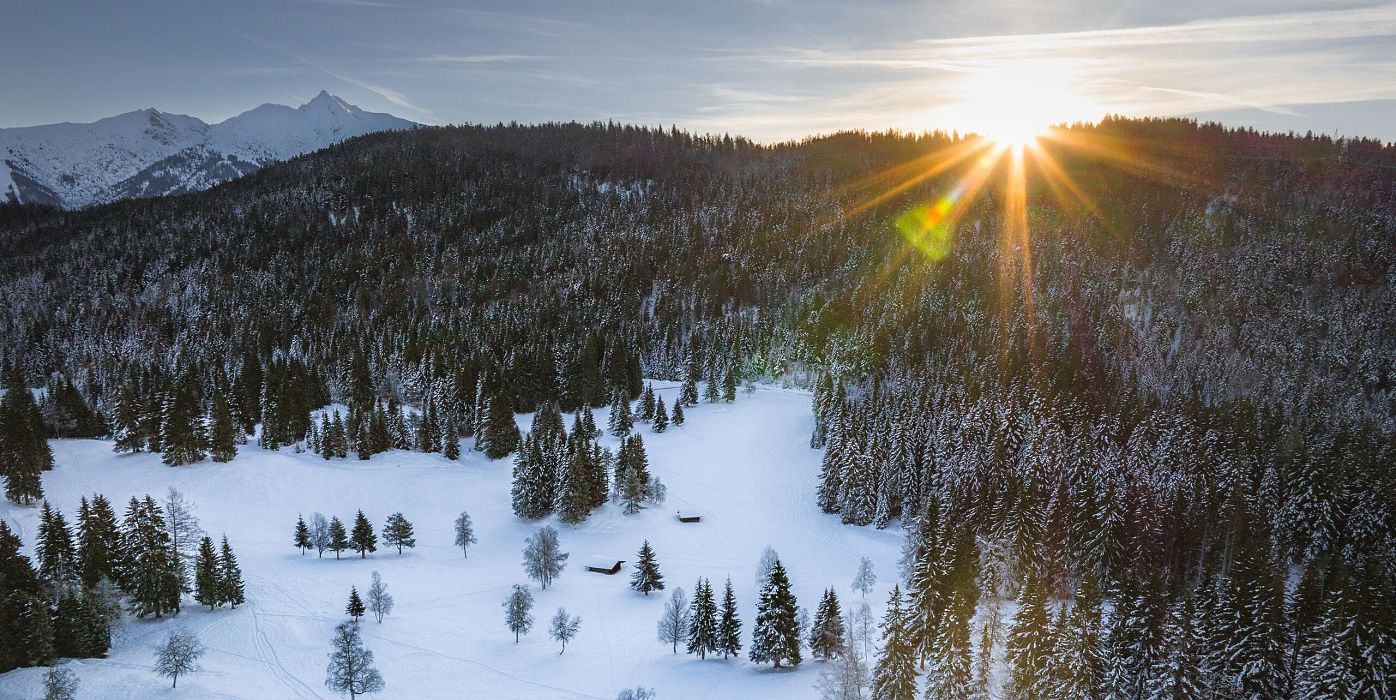 Wildmoos im Winter Drohnenaufnahme Blick Richtung Reither Spitze mit Sonnenstern Bäumen und 2 kleinen Hütten (1)