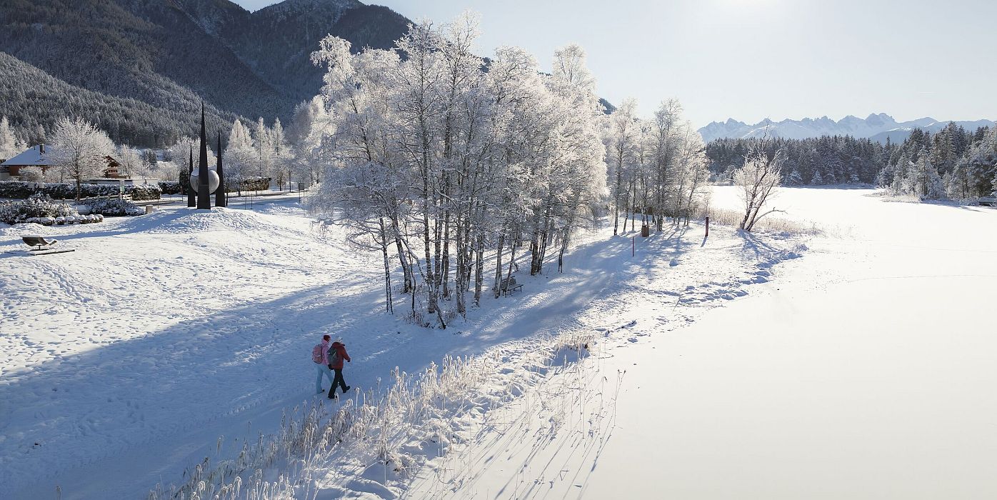 Winterwandern in der Region Seefeld_Drohnenaufnahme_Mann und Frau laufen entlang des Ufers des Wildsees
