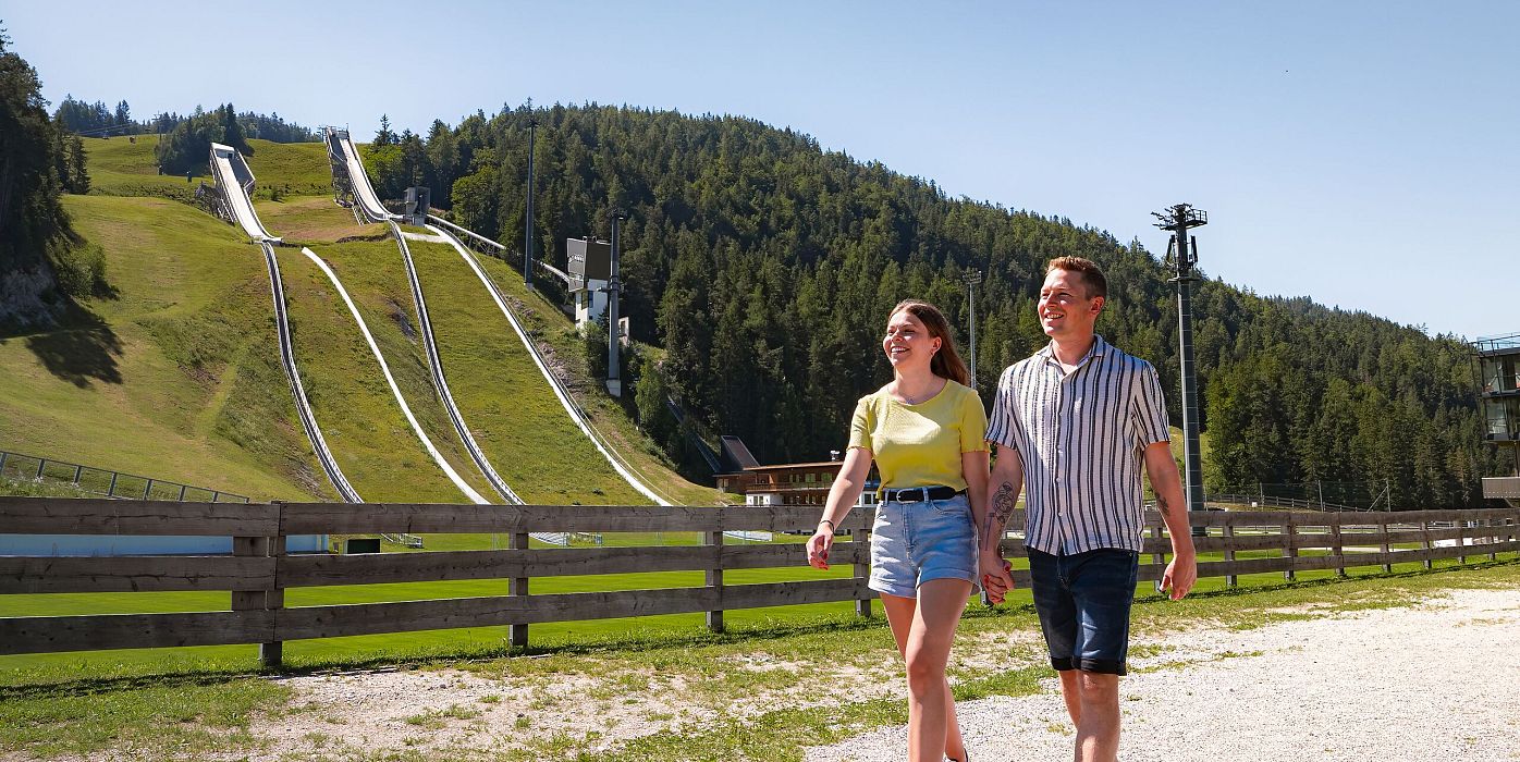 WM Arena im Sommer_Paar läuft durch die Arena_Schanze im Hintergrund