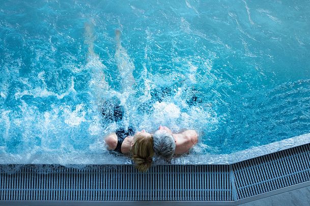 A couple partially submerged in a blue pool, enjoying a moment together.