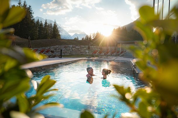 Two people swimming in a pool with mountains and sunset in the background.