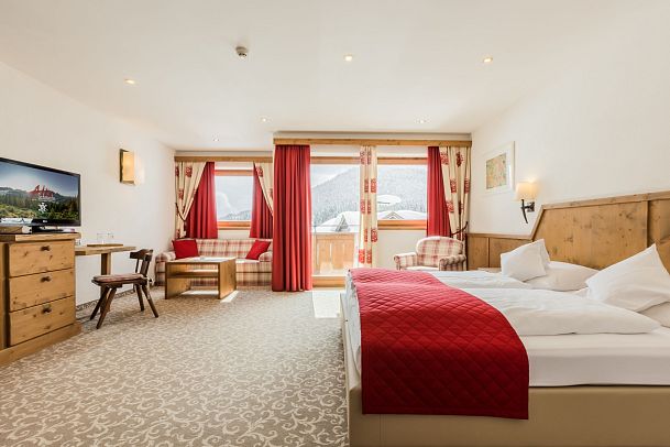 Cozy hotel room with wooden furniture, double bed, seating area, and large windows with scenic views.