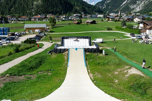 A summer slide in a green field with parked cars and people enjoying the area.