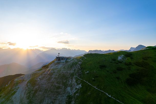 Sonnenuntergang über einem Berggipfel mit Hütte in der Region Seefeld. Sanfte Hügel und Berge im Hintergrund.