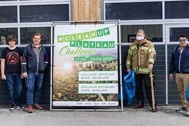 Vier Personen stehen neben einem Banner der "Cleanup Plateau Challenge" vor einer Garage.