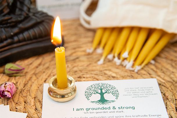 Brennende Kerze, Trockenblumen und eine Karte mit dem Text 'I am grounded & strong' auf einem Tisch.