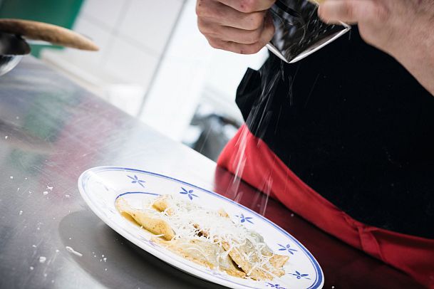 Ein Koch reibt Käse über einen Teller mit Pasta.