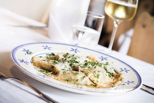 Ein Teller mit gefüllten Teigtaschen, garniert mit Schnittlauch und Käse, neben einem Glas Weißwein.