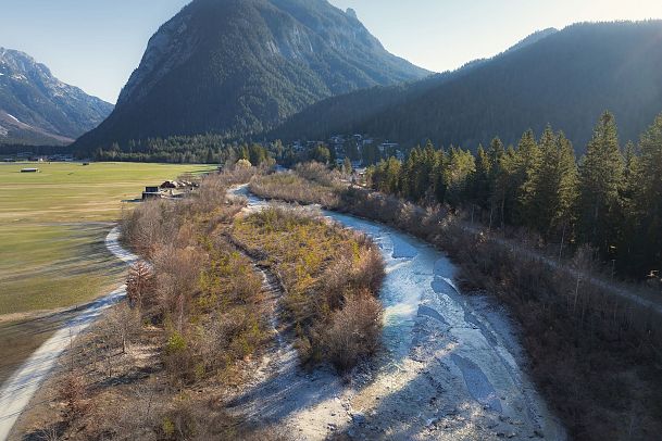 Bach in der Region Seefeld umgeben von Bergen und herbstlicher Natur, bei blauem Himmel.