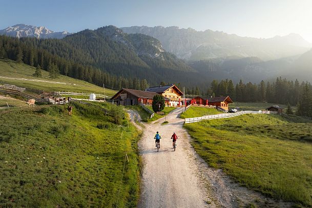 Zwei Wanderer auf einem Bergpfad, Almhütte und Berge im Hintergrund. Outdoor-Abenteuer in der Region Seefeld.