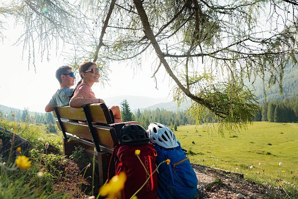 E-Biken im Gaistal im Sommer_zwei Biker_innen fahren bei Morgenstimmung zur Hämmermoosalm_Biker auf Pausenbank