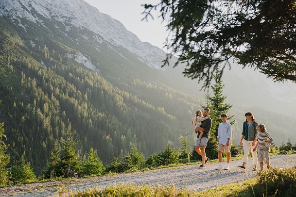 Familie beim Wandern in den Bergen, umgeben von Wald und Bergen.