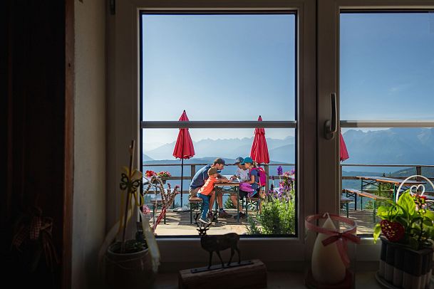 Familien-Weitwanderung im Gaistal - Familie auf der Terasse von Wettersteinhütte schaut auf Wanderkarte - Aufnahme durchs Fenster