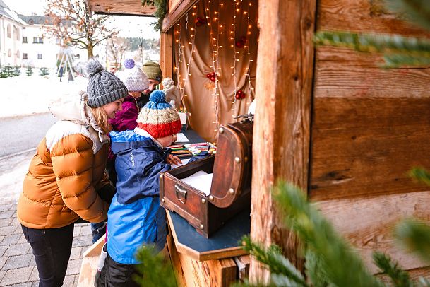 Familie an einem weihnachtlich dekorierten Stand in der Region Seefeld. Kinder betrachten eine Truhe. Winterliche Kleidung.