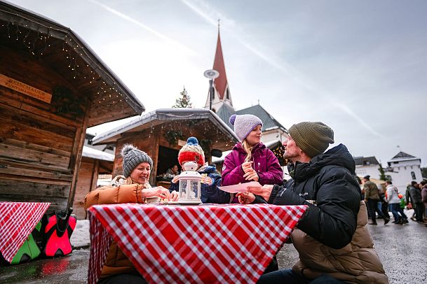 Family at a Christmas market with wooden huts and church tower in background. Winter scene with festive atmosphere.