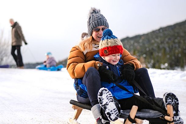 Mother and child sledding in snowy landscape, winter fun.