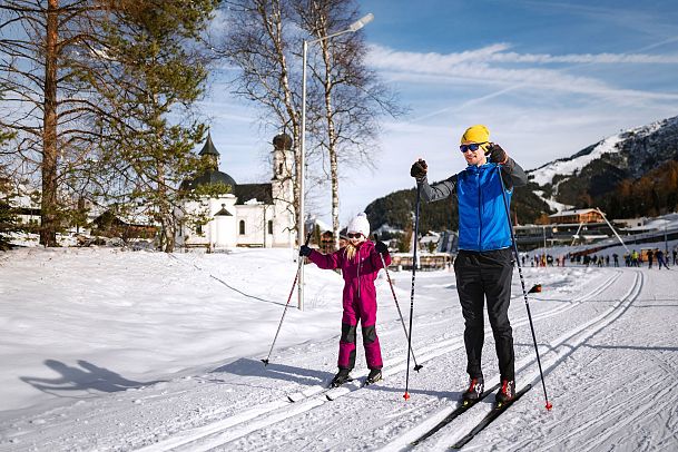 Cross-country skiers in Region Seefeld with chapel and snowy hills in the background.