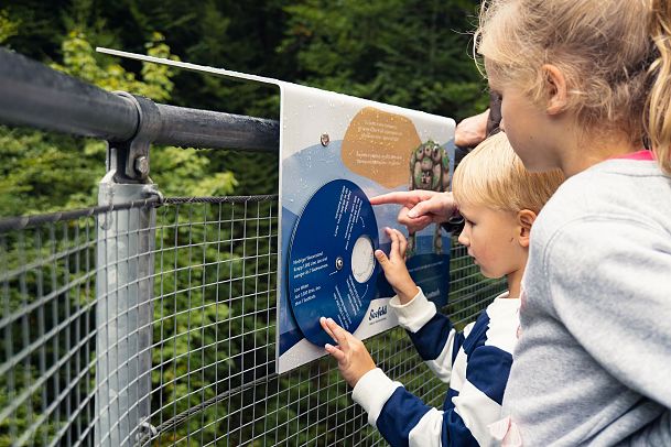 Two children and an adult examining an informational sign near a fence.
