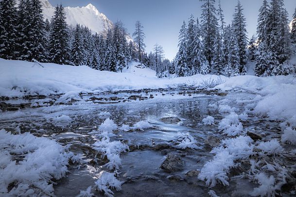 Winterlandschaft mit gefrorenem Fluss und schneebedeckten Bäumen.