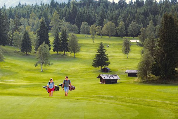 Golfen im GC Wildmoos im Sommer_zwei Golfer laufen über Wiese_Hütten im Hintergrund