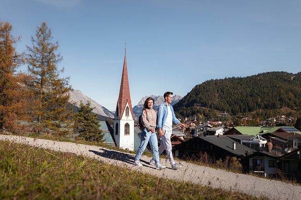 herbstwanderung-in-seefeld-paar-laeuft-auf-weg-am-pfarrhuegel-pfarrkirche-st
