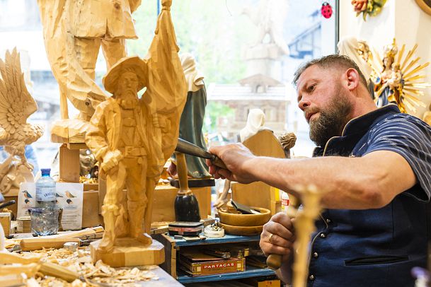 Ein Holzschnitzer arbeitet an einer Statue, umgeben von weiteren Holzskulpturen.