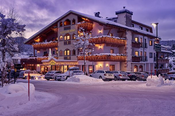 A snowy hotel with warm lighting, traditional design, and festive decorations during dusk.