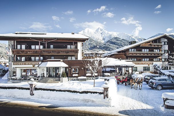 Hotel in a snowy landscape with mountains in the background and parked cars in front.
