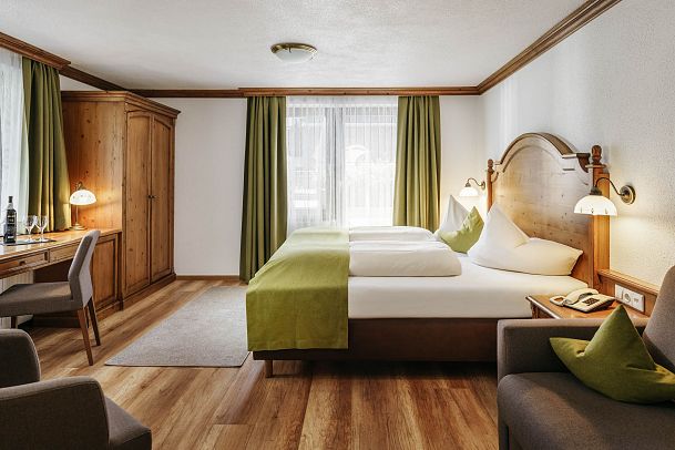 Cozy hotel room with two twin beds, a writing desk, and green curtains.