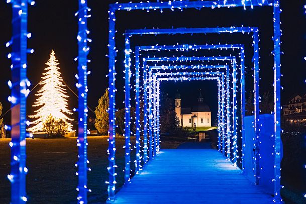 Tunnel aus blauen Lichtern mit festlichem Weihnachtsbaum im Hintergrund.