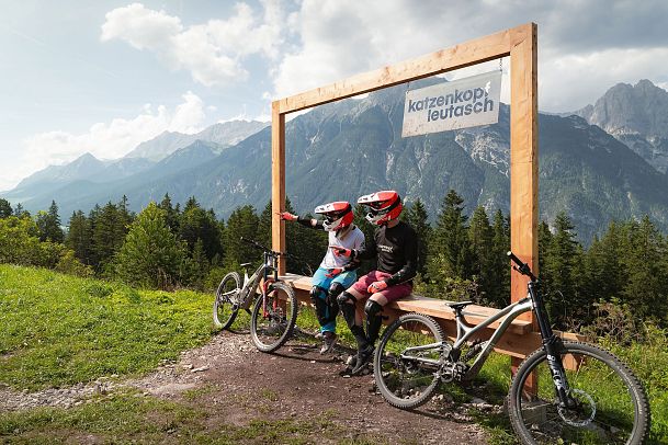 Zwei Mountainbiker sitzen auf einer Bank mit Blick auf die Berge der Region Seefeld.