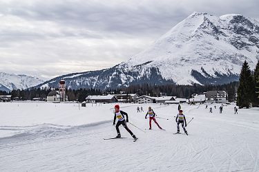 Skifahrer auf einer schneebedeckten Fläche mit Bergen im Hintergrund.