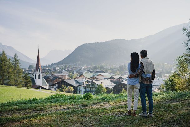 Paar genießt den Ausblick auf die malerische Region Seefeld mit einer Kirche im Vordergrund und Bergen im Hintergrund.