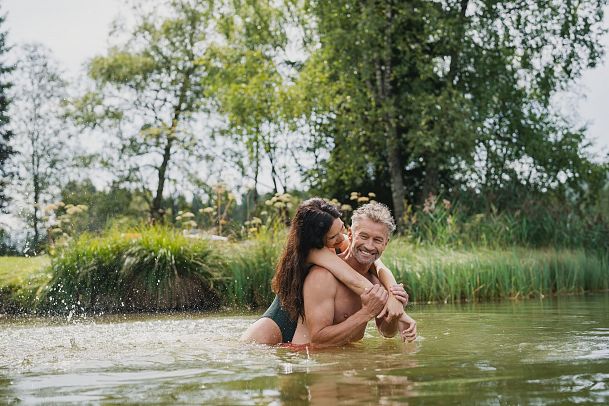 A couple embracing playfully in a pond surrounded by greenery.