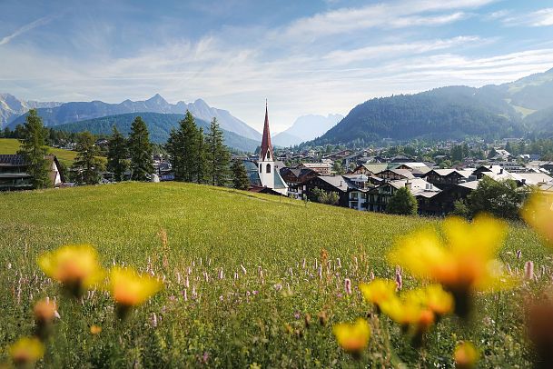 Pfarrhügel Seefeld im Sommer_Blumenwiese und Blick auf Pfarrkirche St. Oswald